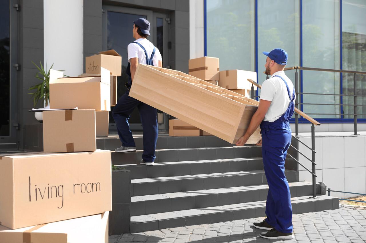 Two Men Carrying a Big Box Over Stairs