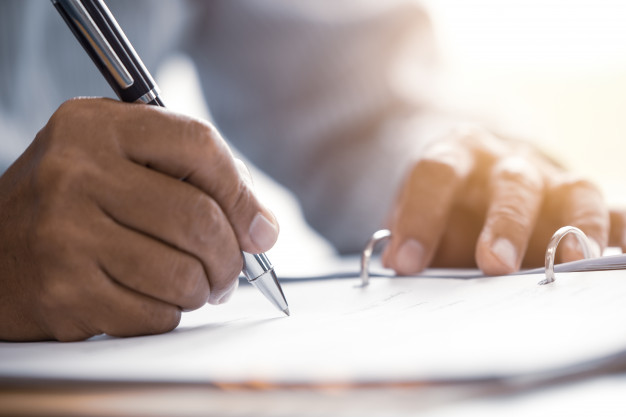 A Man Writing on a Book With a Pen